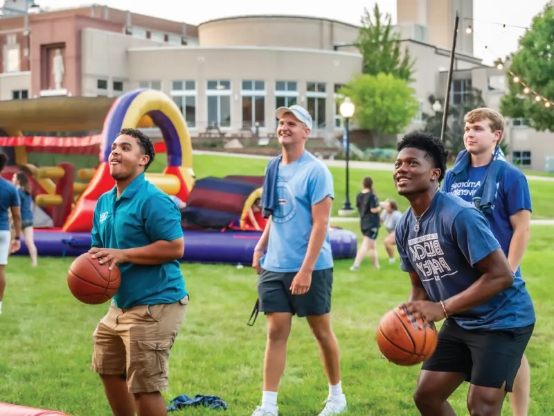 Two students shooting basketballs outside at an evening event.